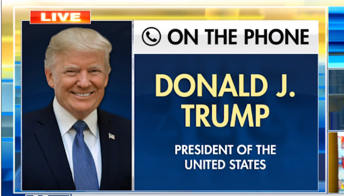 Auf einem großen Bildschirm ist Donald Trump zu sehen, der ein Interview über das Telefon gibt.