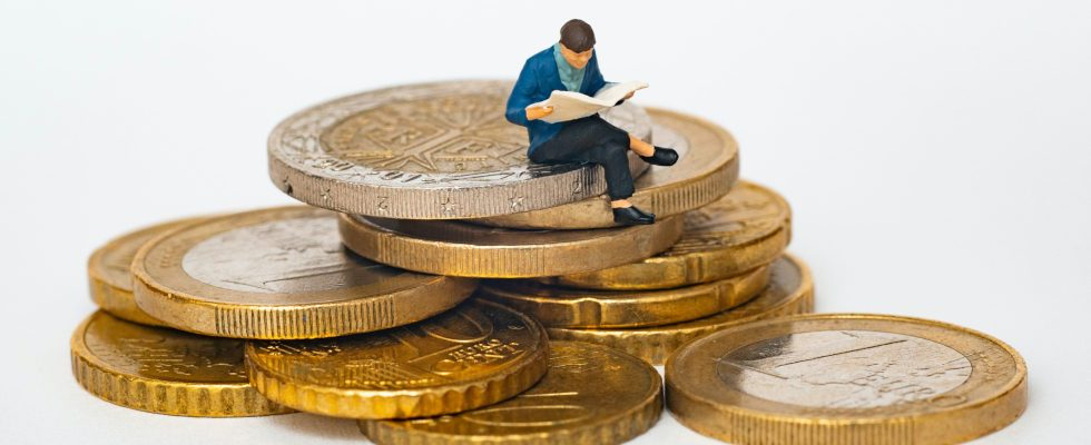 © Mathieu Stern - Unsplash, Figur (Miniatur) sitzt Zeitung lesend auf Euromünzen
