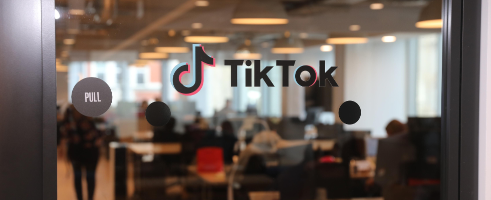 Glastür mit TikTok-Logo und -Schriftzug, Personen verschwommen im Hintergrund