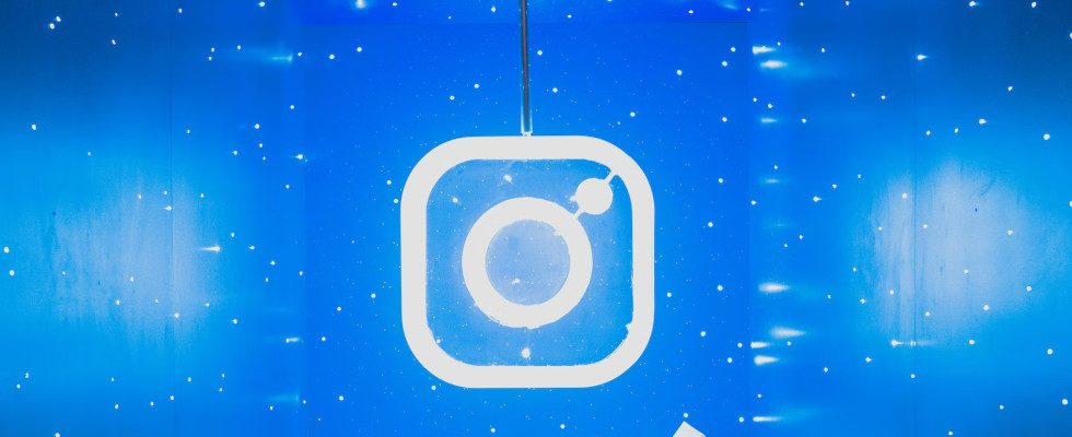 © Lance Matthew Pahang - Unsplash, Instagram-Logo in weiß, neonleuchtend, vor blau-weißem Hintergrund, hängend wie eine Lampe