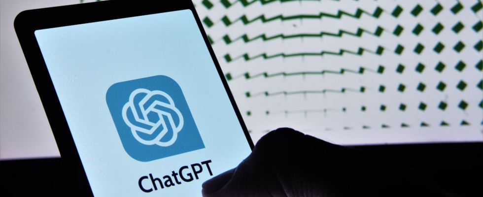 Smartphone in Hand mit ChatGPT-Schriftzug, OpenAI-Grafik im Hintergrund