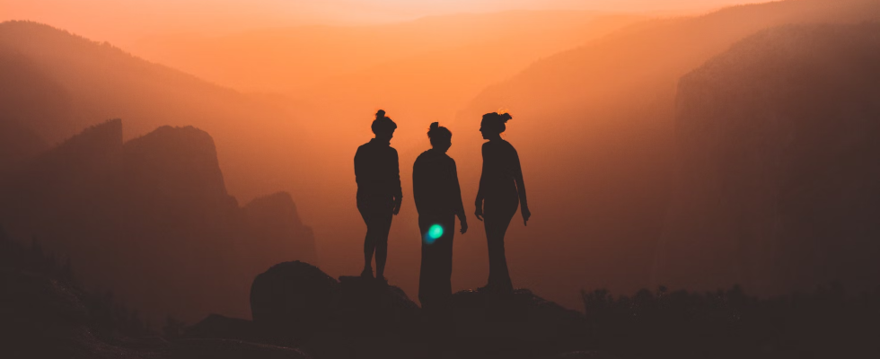 Drei Frauen stehen bei Sonnenuntergang auf einem Berg.