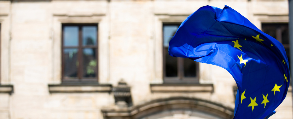 Europaflagge vor Gebäude, © Markus Spiske - Unsplash (Änderungen wurden vorgenommen via Canva)