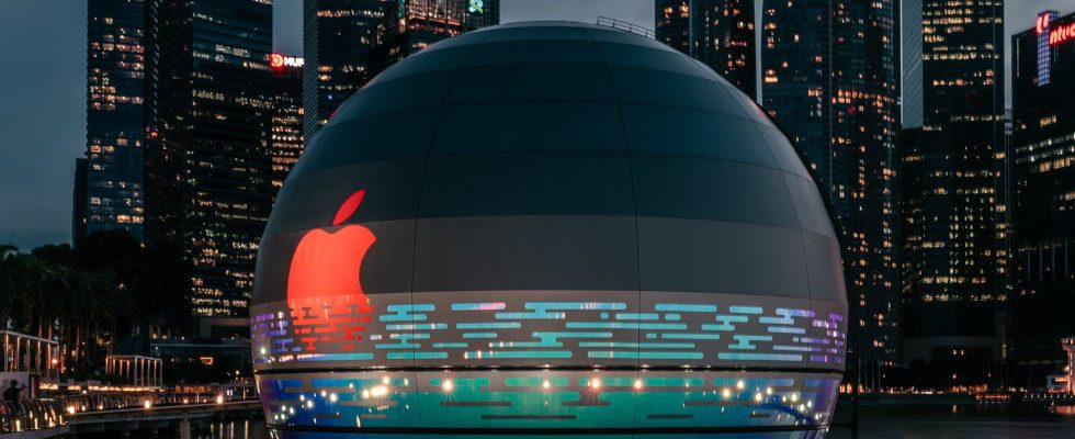 © Keming Tan - Unsplash, Apple-Logo in Rot auf dunkler Kugel vor Skyline (dunkel) einer Großstadt