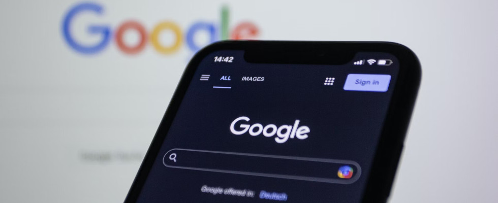 Google auf Smartphone im Darkmode, auf Laptop im Hintergrund