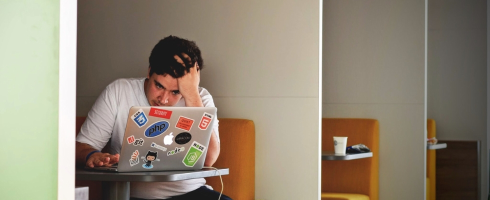 Ein junger Mann sitzt gestresst und verzweifelt vor seinem Laptop.