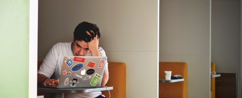 Junger Mann sitzt gestresst vor seinem Laptop und schaut verzweifelt.