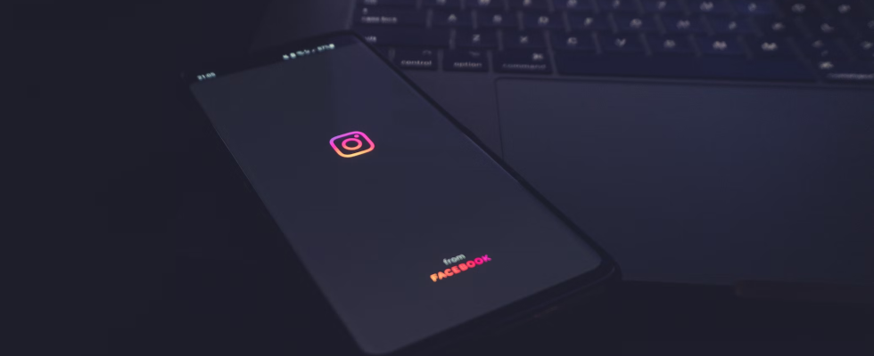 © Azamat E - Unsplash, Instagram-Logo auf Smartphone, schwarzer Hintergrund mit Tastatur