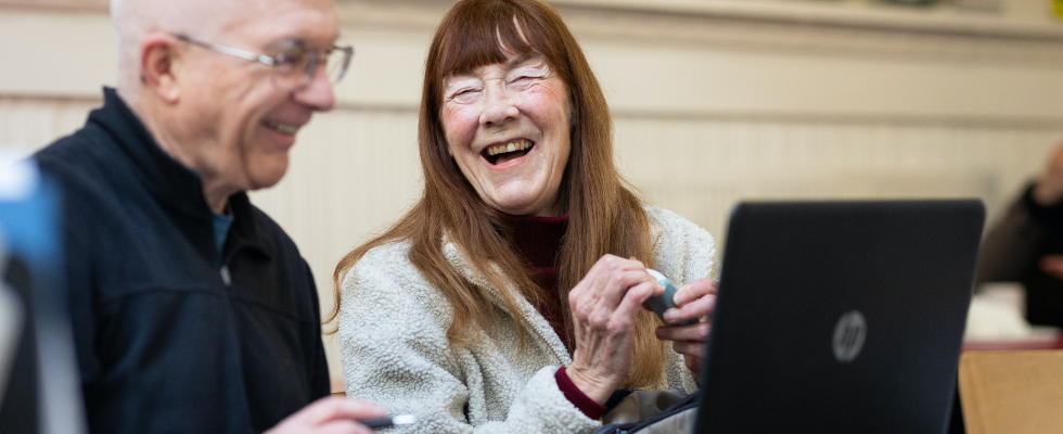 Zwei ältere Menschen sitzen vor ihrem Laptop mit digitalen Tools.