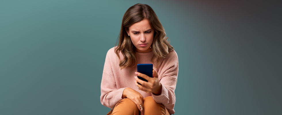 KI-generiertes Bild einer Frau, die vor einem grauen Hintergrund genervt auf ihr Smartphone schaut