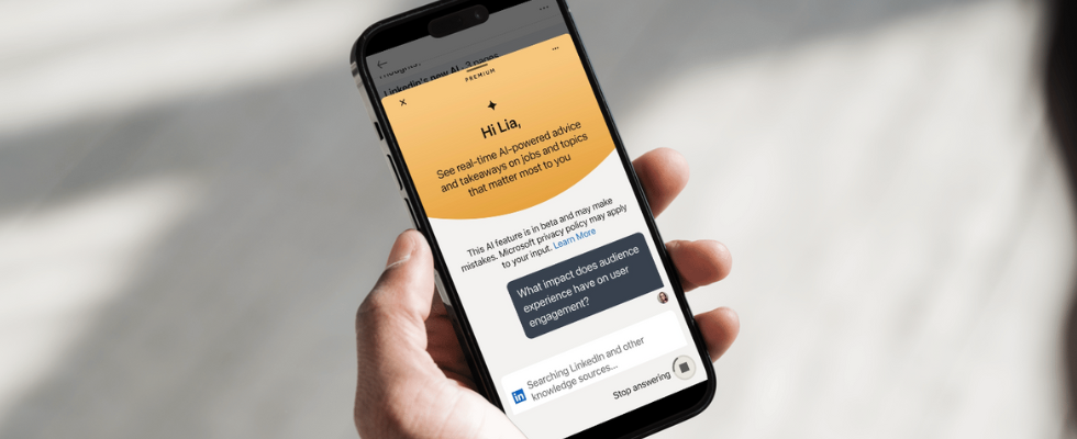 © Lia Habermann (Änderungen vorgenommen via Canva), Hand hält Smartphone. Auf diesem ist LinkedIn und die neue KI-Assistenz im Chat geöffnet.
