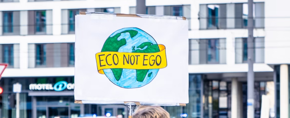 © Mika Baumeister - Unsplash, Eco not Ego-Schriftzug auf Plakat mit Weltkugel darauf, vor Häusern