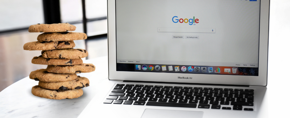 © pixelshot, Billion Photos via Canva, Laptop mit Google-Startseite, Cookies auf Tisch gestapelt