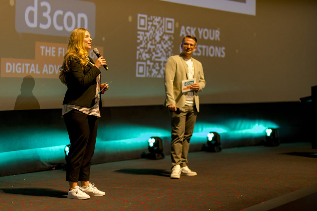 Tessa Stamer und Robert Fey eröffnen den Conference Day der d3con 2025, © d3con, zwei Personen mit Mikrofonen auf der Bühne im Kino 