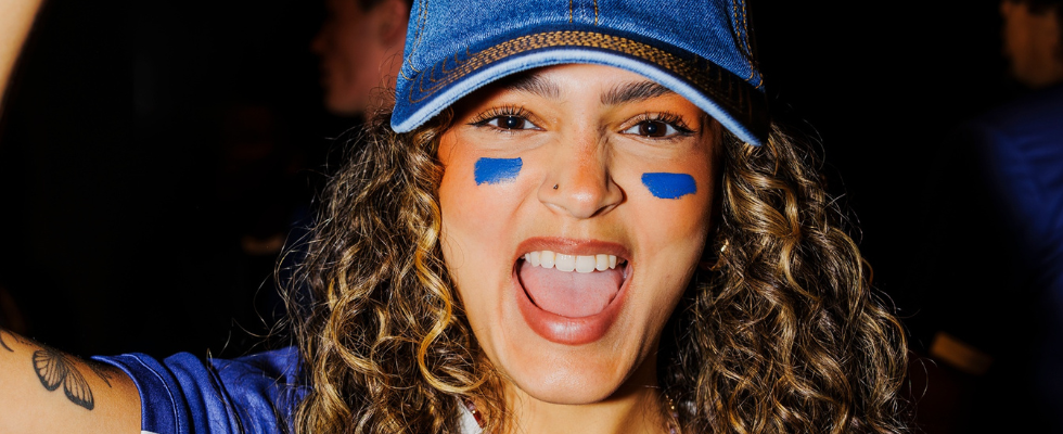 Frau mit Denim Cap und blauer Schminke unter Augen jubelt