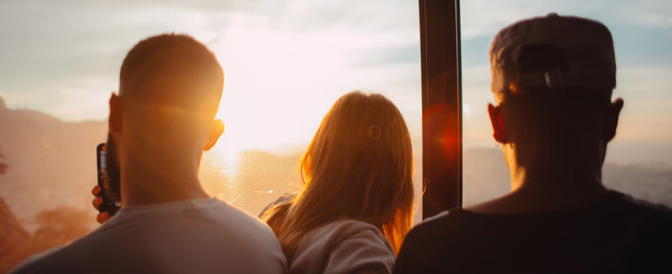 Mehrere Menschen schauen aus einem Fenster und bestaunen den Sonnenuntergang. Link zum Artikel: Die Top 10 der Sommerjobs: Wo das Gehalt und die Zufriedenheit am höchsten sind