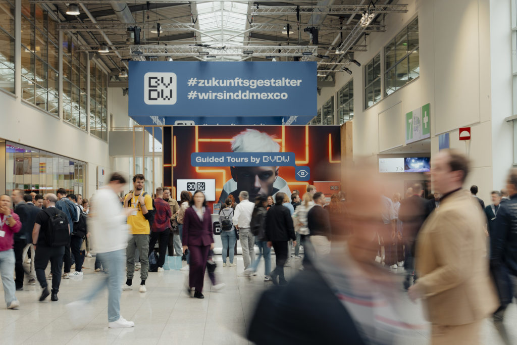 Menschen laufen in Kölnmesse in Gängen herum, Plakate des BVDW mit Schriftzügen im Hintergrund 