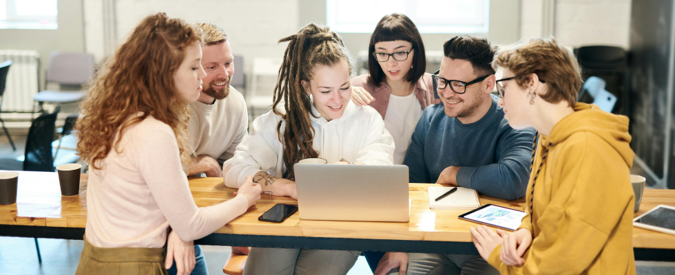 Mehrere Angestellte sitzen gemeinsam in einem Büro um einen Laptop herum