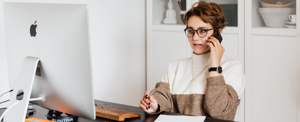 Eine Frau sitzt an ihrem Bürotisch und telefoniert mit einem Handy in der Hand. Neuer Artikel: Fast 6 von 10 Beschäftigten erledigen Privates im Job – und fühlen sich produktiver